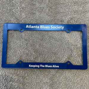 A blue ABS license plate frame for the Atlanta Blues Society with the slogan "keeping the blues alive," laid on a grey carpeted surface.
