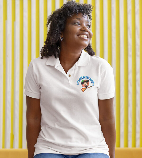 Woman in embroidered polo shirt smiling and looking to the side against a yellow striped background.